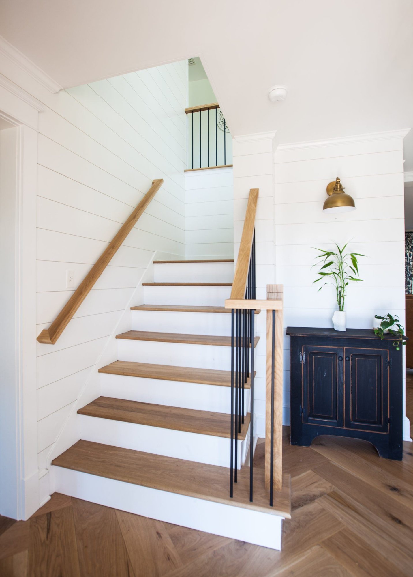 A modern staircase with wooden steps and white shiplap walls in a whole house remodel by Craft Design + Build in Essex, Connecticut
