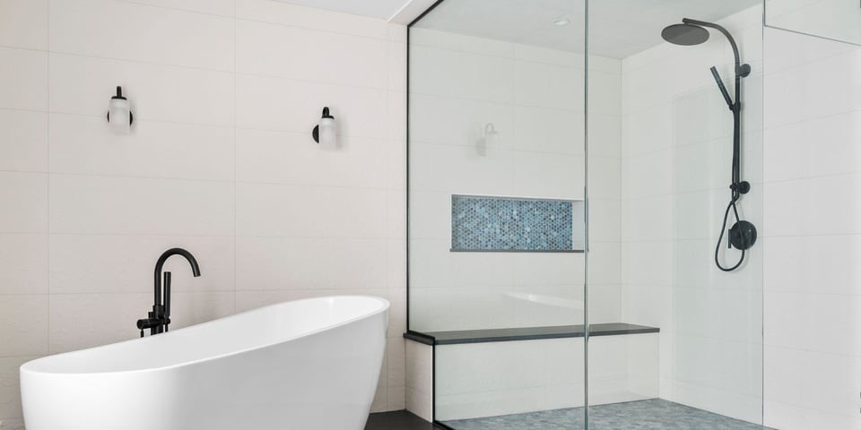 Bathroom remodel in Essex, Connecticut with freestanding white tub, walk in shower with bench, and sleek black and white design