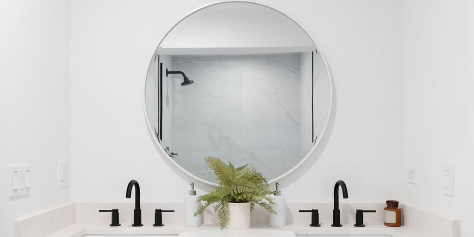 White Bathroom Remodel with Black Sink Fixtures and a Round Mirror