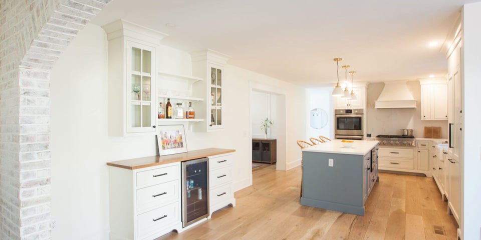 Coastal kitchen remodel in Connecticut with brick archway, white cabinets, kitchen island with seating, and light wood floors