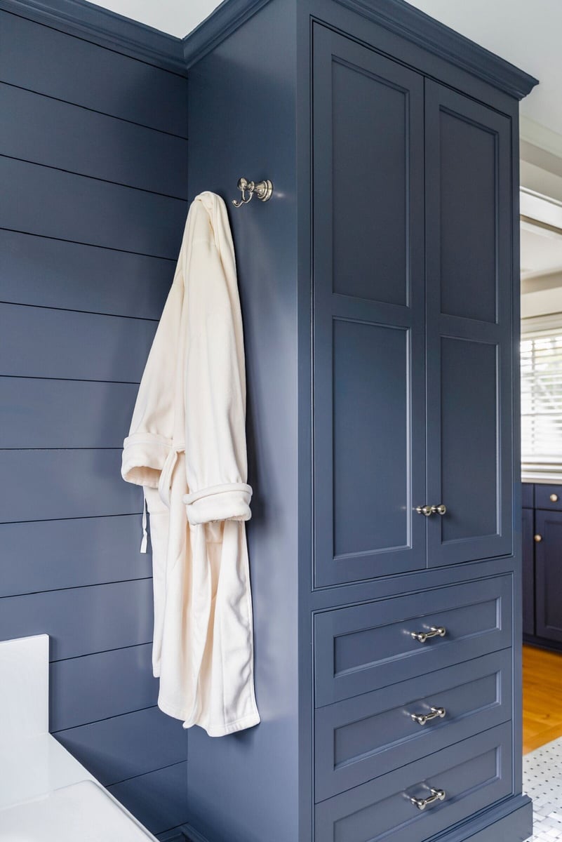 Cream bathrobe hanging on navy blue bathroom cabinet in Essex Primary Bathroom by Craft Design + Build, Essex, Connecticut