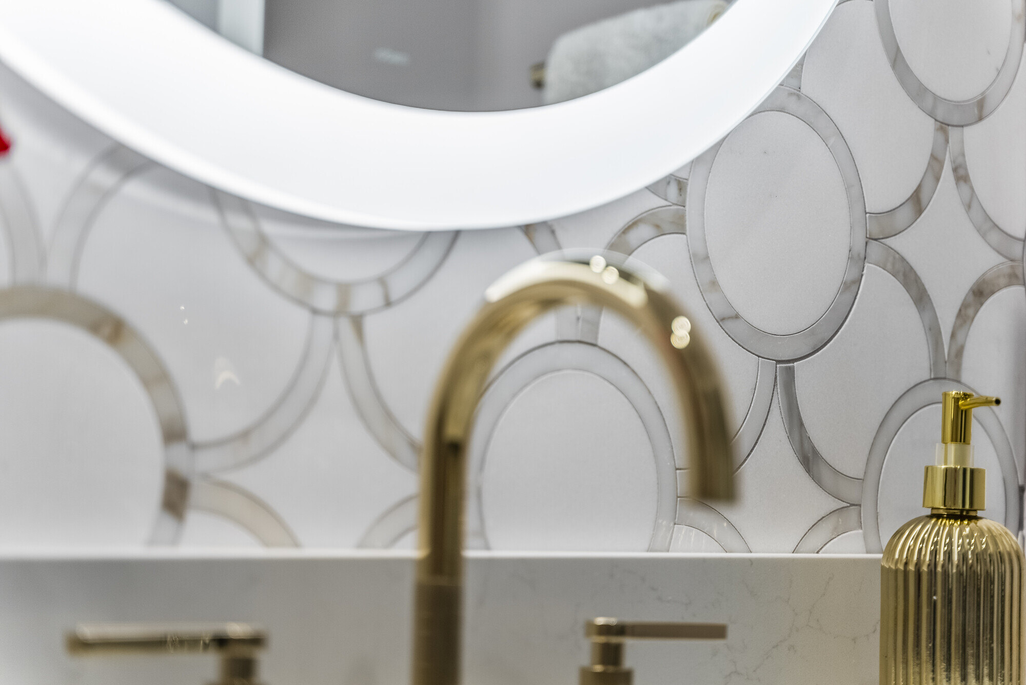 Close-up of a modern bathroom vanity with gold fixtures and lighted mirror by Craft Design Build in Essex, CT