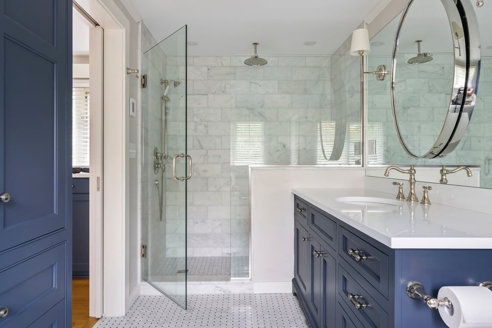 custom bathroom remodel in essex connecticut with blue cabinets, white tile and countertops, and a large glass door shower with marble tile