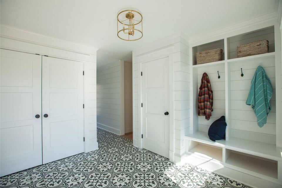 custom-designed mudroom with black and white patterned ceramic tile, white shiplap walls, and custom shelving and hooks