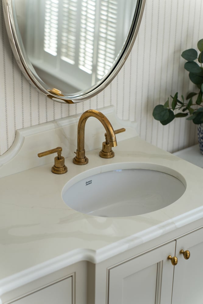 detailed bathroom sink with gold fixtures and oval mirror in custom home by Craft Design + Build in Westbrook, CT