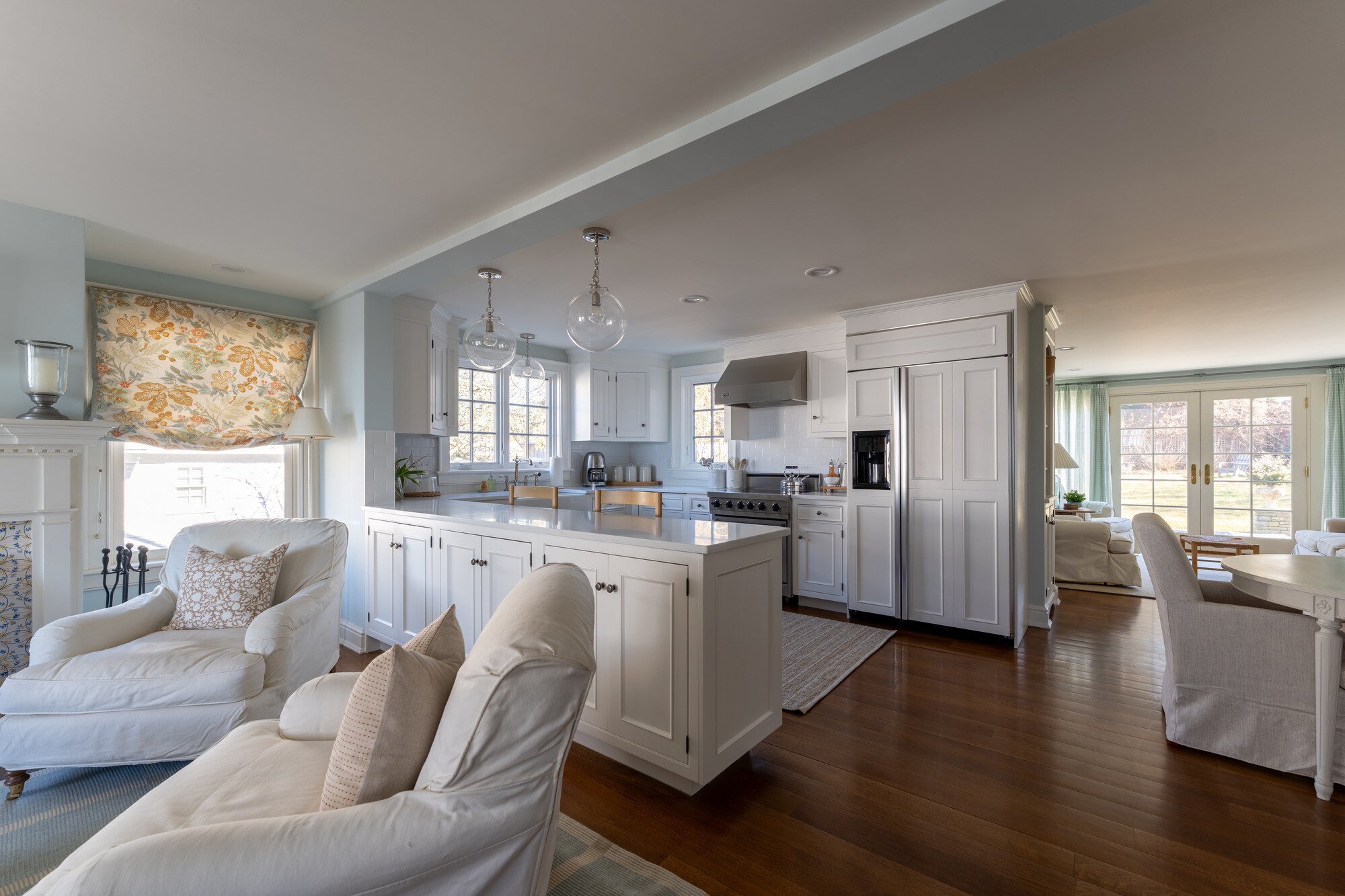 Open-plan living and kitchen area with floral window treatments by Craft Design Build, Essex, CT