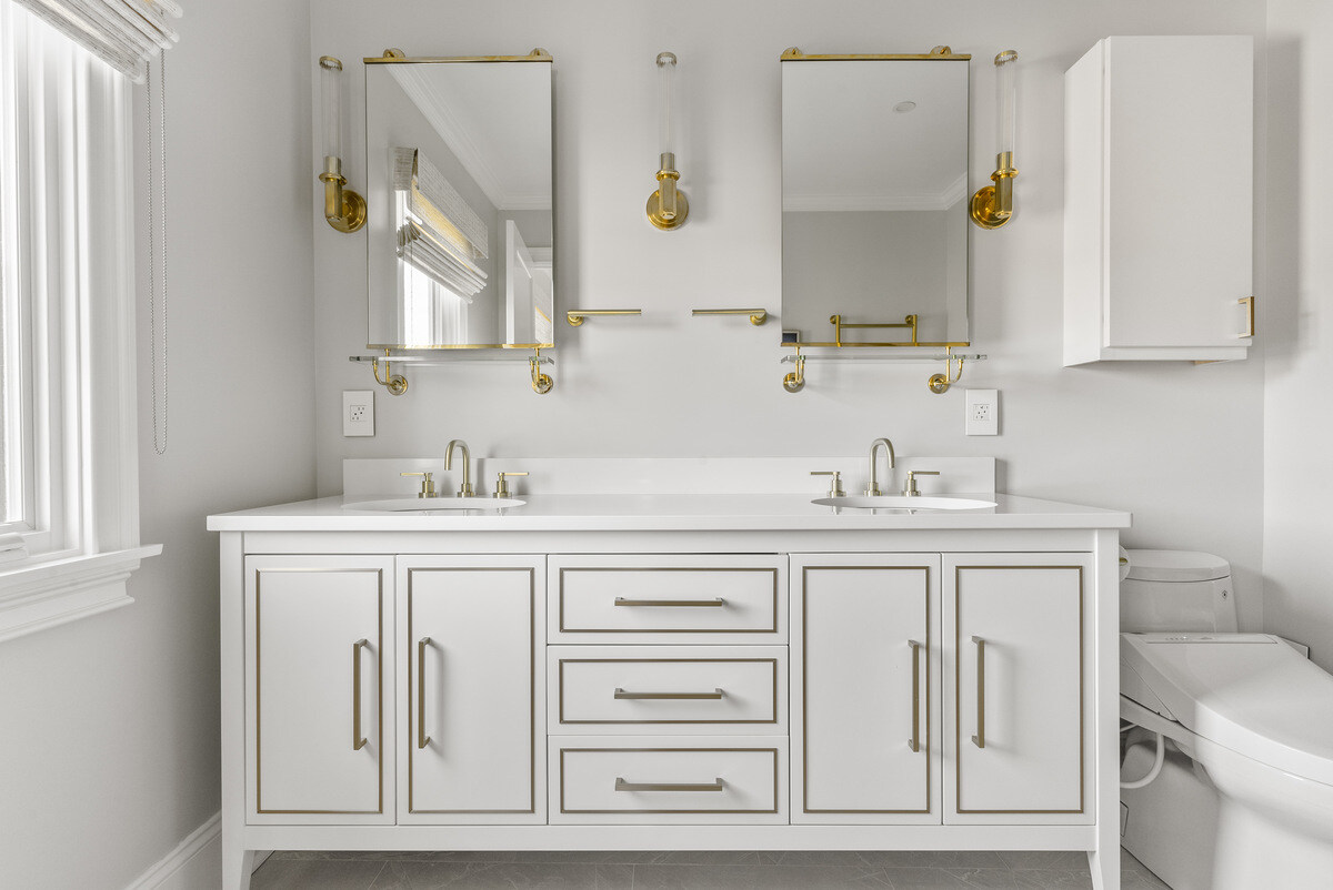 Double vanity bathroom with gold fixtures and ample light by Craft Design Build in Essex, CT
