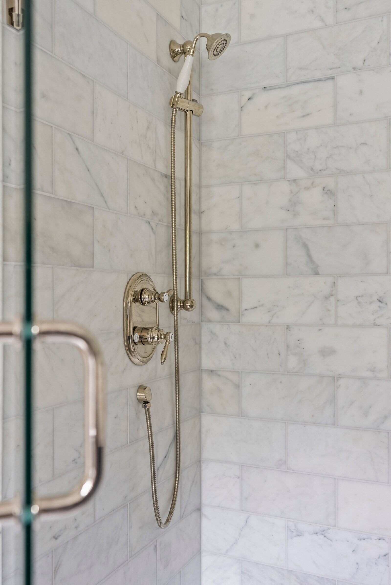 Marble shower with elegant brass fixtures in an Essex Primary Bathroom remodel by Craft Design + Build in Essex, Connecticut